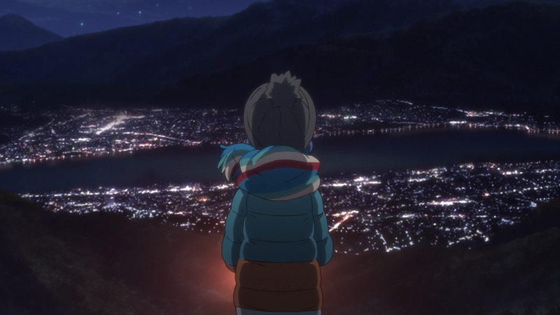 A screenshot from the first season of the Yuru Camp anime, wherein a girl bundled in warm outdoor clothing gazes over a vista at night to see the down below outlined by tiny street-lights, framed by the mountains behind and a river running through it.